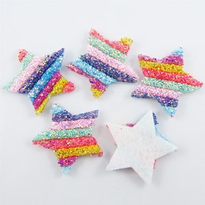 May include: Five colourful glitter star-shaped embellishments. Four stars are multi-coloured with a rainbow stripe pattern. One star is white.