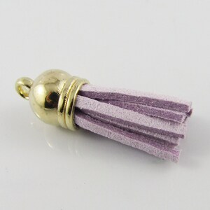 May include: A small, light purple tassel with a gold metal top. The tassel is made of soft, suede-like material and has a loop at the top for attaching to a keychain or other item.