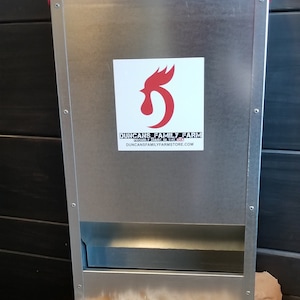 May include: A red and silver metal chicken feeder with a white sticker that says "Duncan's Family Farm - Proudly Made in the USA - duncansfamilyfarmstore.com".