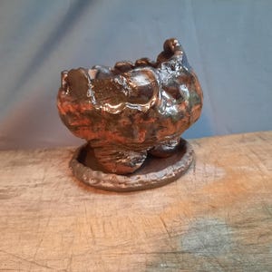 Peut inclure: Un petit pot en céramique rustique de couleur brune avec une surface texturée. Le pot est posé sur une surface en bois.