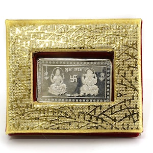Puede incluir: Una placa rectangular plateada con imágenes de Lakshmi y Ganesha, deidades hindúes, rodeada de un marco dorado. La placa está inscrita con el texto "Shubh Labh" en hindi, que se traduce como "Buena Fortuna".