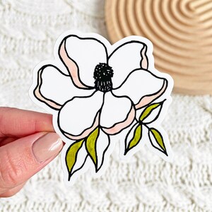 May include: A white flower with pink accents and green leaves. The flower is drawn in a simple, stylized manner.