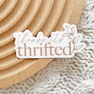 May include: White sticker with brown text that reads "thanks it's thrifted". A simple line drawing of a leafy branch is to the right of the text.