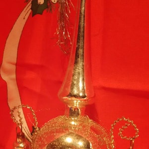 Peut inclure: Un sommet d'arbre de No&euml;l argent&eacute; avec une boule ronde en miroir et trois cloches qui pendent. Le sommet est d&eacute;cor&eacute; de paillettes dor&eacute;es.