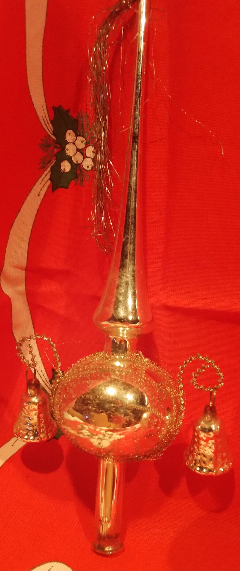 Peut inclure: Un sommet d'arbre de No&euml;l argent&eacute; avec une boule ronde en miroir et trois cloches qui pendent. Le sommet est d&eacute;cor&eacute; de paillettes dor&eacute;es.