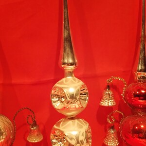 Peut inclure: Trois sommets d'arbre de No&euml;l vintage en verre. L'un est argent&eacute; avec deux bulbes ronds et un sommet pointu. Les deux autres sont rouges et argent&eacute;s avec un bulbe rond et un sommet pointu. Chaque sommet a une petite cloche qui pend.