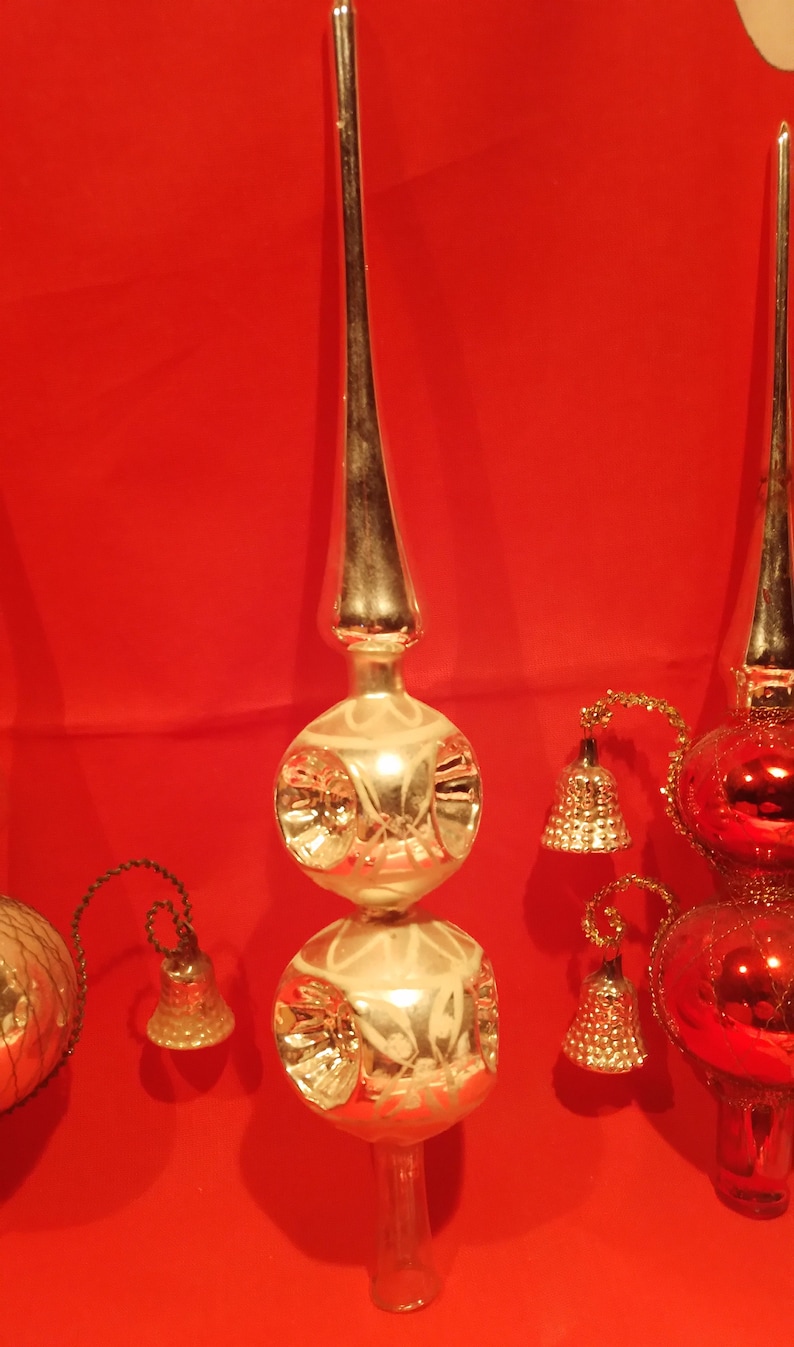 Peut inclure: Trois sommets d'arbre de No&euml;l vintage en verre. L'un est argent&eacute; avec deux bulbes ronds et un sommet pointu. Les deux autres sont rouges et argent&eacute;s avec un bulbe rond et un sommet pointu. Chaque sommet a une petite cloche qui pend.