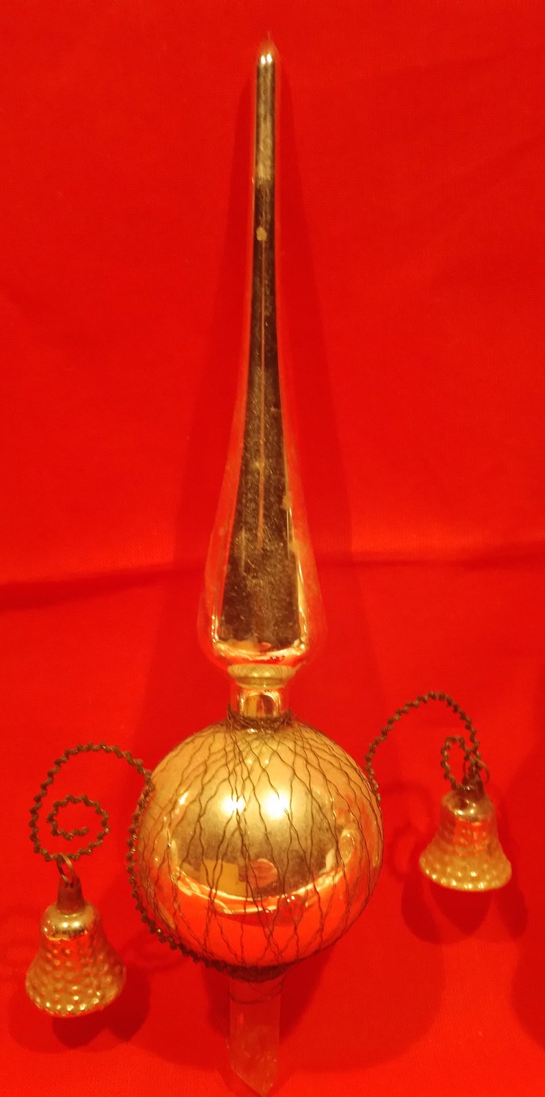 Peut inclure: Un sommet d'arbre de No&euml;l vintage en verre avec une finition argent&eacute;e et un motif en maille de fil. Le sommet a trois cloches attach&eacute;es &agrave; lui avec des cordons noirs.