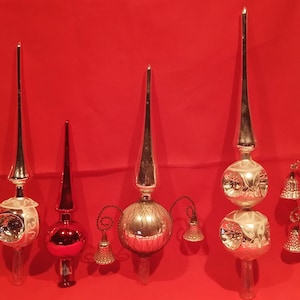 Peut inclure: Six d&eacute;corations de sommet d'arbre de No&euml;l en verre vintage dans diff&eacute;rents styles. Les sommets sont en verre argent&eacute;, rouge et transparent avec des cloches et un sommet pointu. Les sommets sont affich&eacute;s sur un fond rouge.