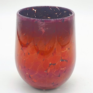 Puede incluir: Un jarrón de vidrio rojo y morado con una superficie moteada y texturizada. El jarrón tiene un fondo redondeado y una abertura ancha.