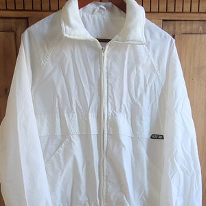 May include: White windbreaker jacket with a zipper closure and a fleece-lined collar. The jacket has a black logo that says "Pacific Trail".