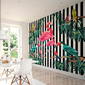 May include: A white dining room with a black and white striped wallpaper featuring pink flamingos and tropical birds. The wallpaper has green palm leaves and black branches. The room has a white table and chairs.