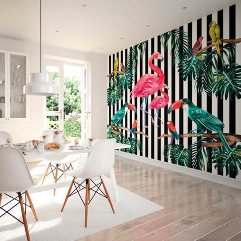 May include: A white dining room with a black and white striped wallpaper featuring pink flamingos and tropical birds. The wallpaper has green palm leaves and black branches. The room has a white table and chairs.
