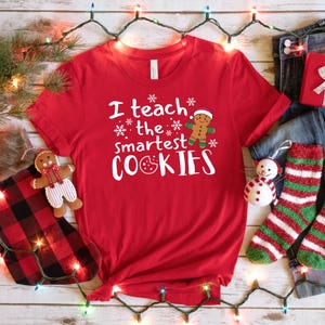 May include: Red t-shirt with white text that says "I teach the smartest cookies" and a gingerbread man graphic.