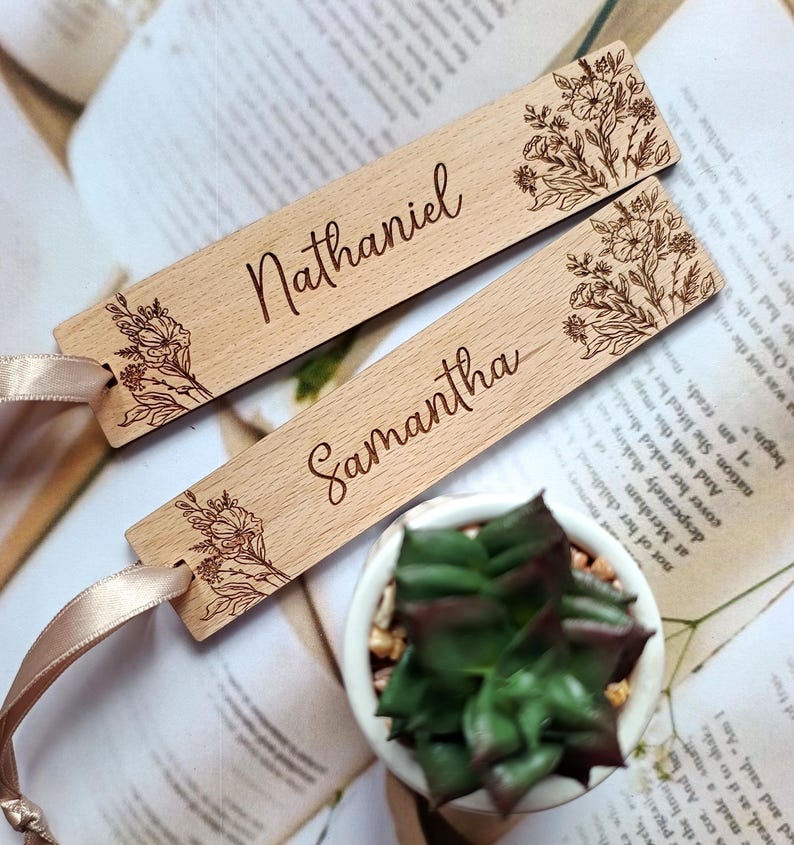 May include: Two wooden bookmarks with floral designs and personalized names, "Nathaniel" and "Samantha", with a beige ribbon attached to one bookmark.