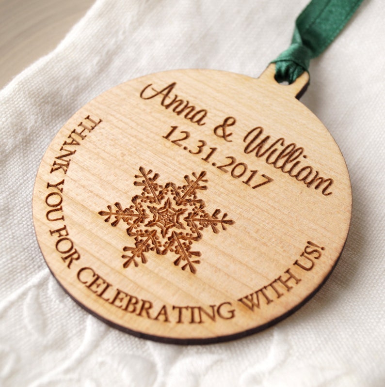 May include: A round wooden ornament with a snowflake design and the text "Anna & William 12.31.2017 Thank you for celebrating with us!"