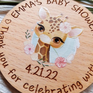 Peut inclure: Une pancarte ronde en bois avec une illustration de girafe, des fleurs et le texte "Emma's Baby Shower" et "Thank you for celebrating with us 4.21.22".
