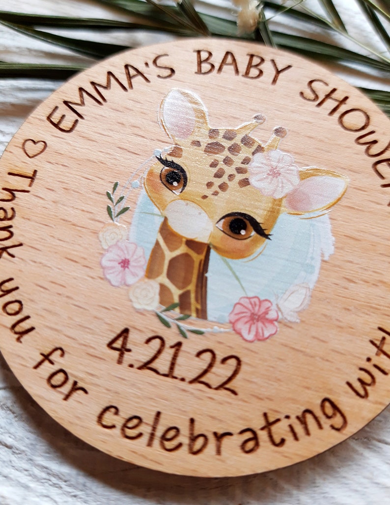 Peut inclure: Une pancarte ronde en bois avec une illustration de girafe, des fleurs et le texte "Emma's Baby Shower" et "Thank you for celebrating with us 4.21.22".