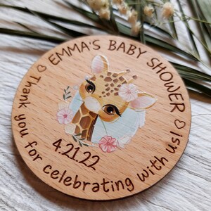 Peut inclure: Une pancarte ronde en bois avec une illustration de girafe et le texte "Emma's Baby Shower is 4.21.22 Thank you for celebrating with us."