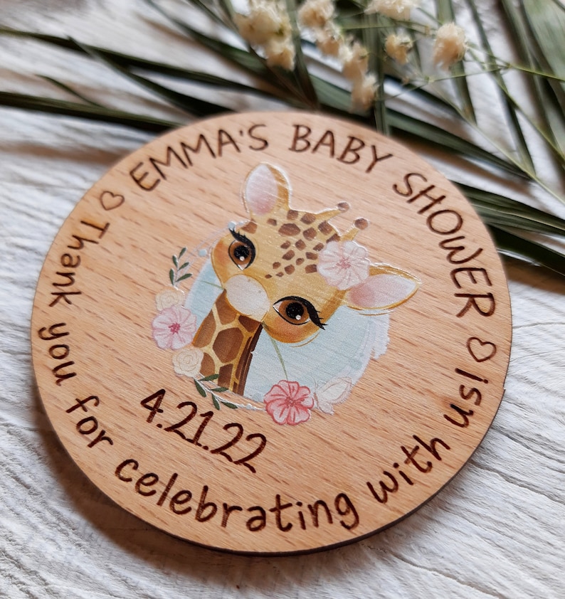 Peut inclure: Une pancarte ronde en bois avec une illustration de girafe et le texte "Emma's Baby Shower is 4.21.22 Thank you for celebrating with us."
