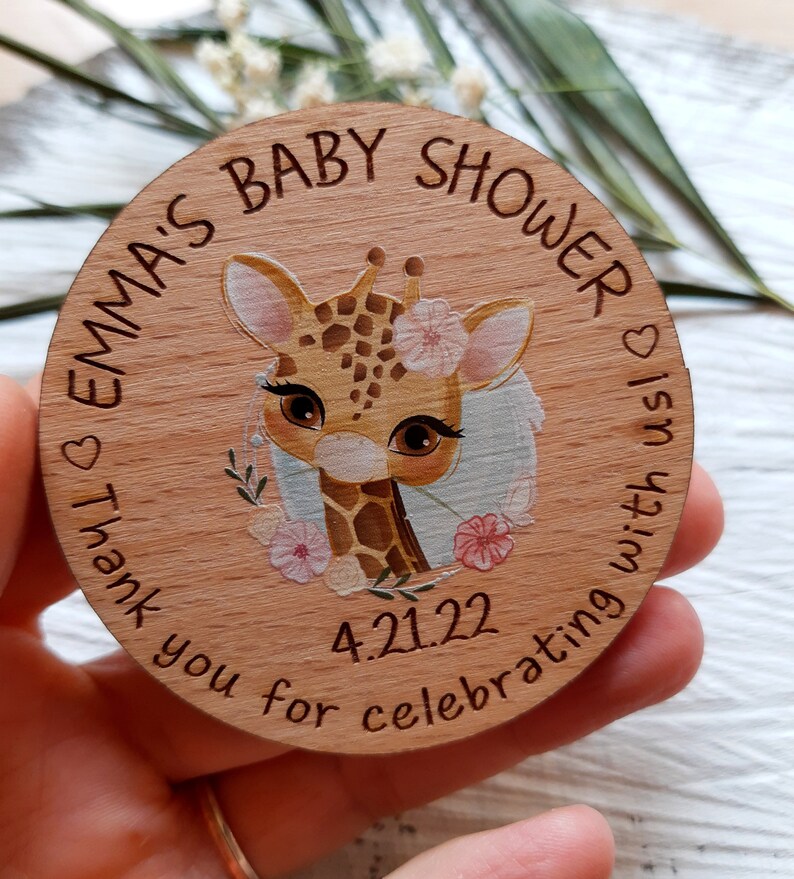 Peut inclure: Une pancarte ronde en bois avec une illustration de girafe et le texte "Emma's Baby Shower" et "Thank you for celebrating with us!" La date "4.21.22" est &eacute;galement incluse sur la pancarte.