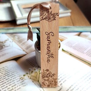 May include: A wooden bookmark with a floral design and the name "Samantha" engraved on it. The bookmark has a light brown ribbon attached to it.