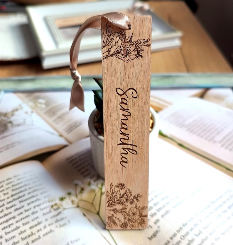 May include: A wooden bookmark with a floral design and the name "Samantha" engraved on it. The bookmark has a light brown ribbon attached to it.
