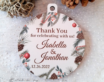 Puede incluir: Adorno redondo de madera con fondo blanco y diseño invernal. El adorno presenta ramas de pino, piñas, bayas rojas y bastones de caramelo. El texto "Thank You for celebrating with us! Isabella & Jonathan 12.26.2022" está impreso en marrón en el adorno.