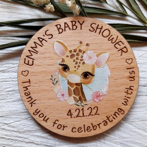 Peut inclure: Une pancarte ronde en bois avec le texte "Emma's Baby Shower" et une adorable girafe de dessin anim&eacute; avec des fleurs. La date "4.21.22" est &eacute;galement incluse sur la pancarte. La pancarte est parfaite pour une f&ecirc;te pr&eacute;natale.