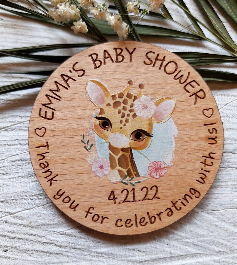 Peut inclure: Une pancarte ronde en bois avec le texte "Emma's Baby Shower" et une adorable girafe de dessin anim&eacute; avec des fleurs. La date "4.21.22" est &eacute;galement incluse sur la pancarte. La pancarte est parfaite pour une f&ecirc;te pr&eacute;natale.