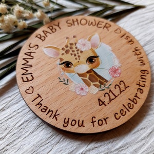 Peut inclure: Une pancarte ronde en bois avec une illustration de girafe, des fleurs et le texte "Emma's Baby Shower is in celebrating with 4.2.122 Thank you for celebrating with us".