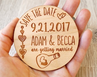 May include: Round wooden save the date magnet with the text "Save the Date 9.21.2017 Adam & Becca are getting married" and a heart in a bottle illustration.