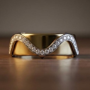 May include: A gold band ring featuring a distinctive wave-shaped top edge. The curved upper border is encrusted with a row of small, clear, round-cut stones that follow the undulating contour of the metal, creating a decorative accent.