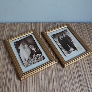 Könnte beinhalten: Zwei rechteckige goldfarbene Bilderrahmen mit weißem Passepartout, die jeweils ein schwarz-weißes Vintage-Foto enthalten. Ein Rahmen zeigt ein Hochzeitsporträt, der andere ein Paar, das zusammen in formeller Kleidung steht.