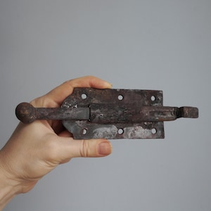 Peut inclure: Un ancien verrou de porte en métal rouillé. Le verrou présente une base rectangulaire avec des trous de vis, une barre coulissante et une poignée ronde. Le métal montre des signes d'usure et de vieillissement.