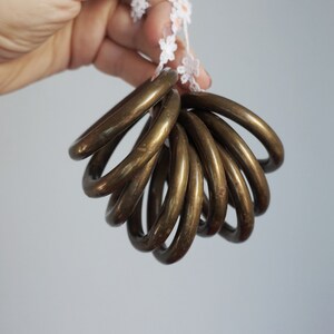 Op de afbeelding: Een verzameling cirkelvormige koperen ringen met een gepolijste metalen afwerking, geregen aan een dun wit koord met kleine, delicate witte bloemvormige versieringen. De ringen zijn glad, afgerond en uniform in hun metalen kleur.