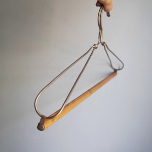 Puede incluir: Una percha de metal plateado con una barra de madera. La percha tiene un gancho en la parte superior y está diseñada para sostener ropa.