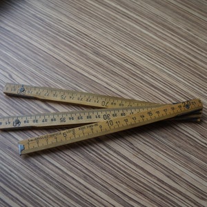 Righello pieghevole in legno beige, asta di misurazione articolata lunga un metro, attrezzo da falegname vintage, arredamento rustico per officina o casa