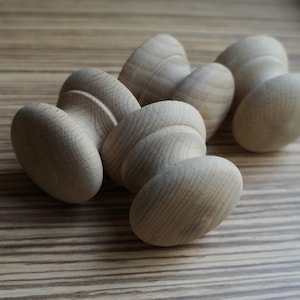 May include: A collection of unfinished wooden knobs, likely for furniture or cabinetry. The knobs have a rounded, mushroom-like shape with a textured surface, and are arranged on a light brown wooden surface. The natural wood grain is visible.