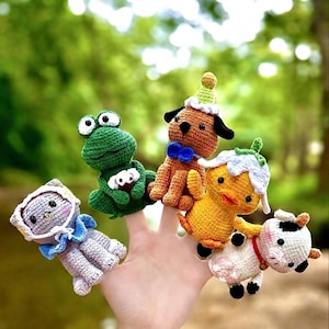 Peut inclure: Un ensemble de cinq marionnettes à doigt crochetées comprenant un chat gris avec un bonnet, une grenouille verte, un chien marron avec un chapeau de fête et un nœud papillon bleu, un canard jaune avec un chapeau fleur et une vache blanche à taches noires.