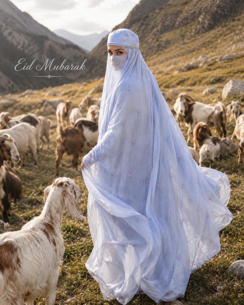 May include: A light blue abaya with a matching head covering and face veil, featuring delicate floral embroidery throughout the fabric. The garment is long and flowing, with the text Eid Mubarak visible in the upper left corner of the image.