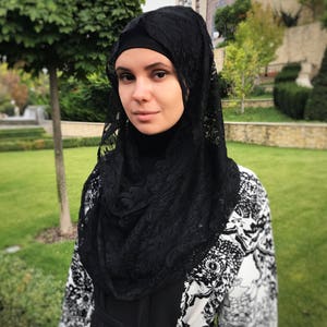 May include: A woman wearing a black lace hijab and a black and white patterned abaya.