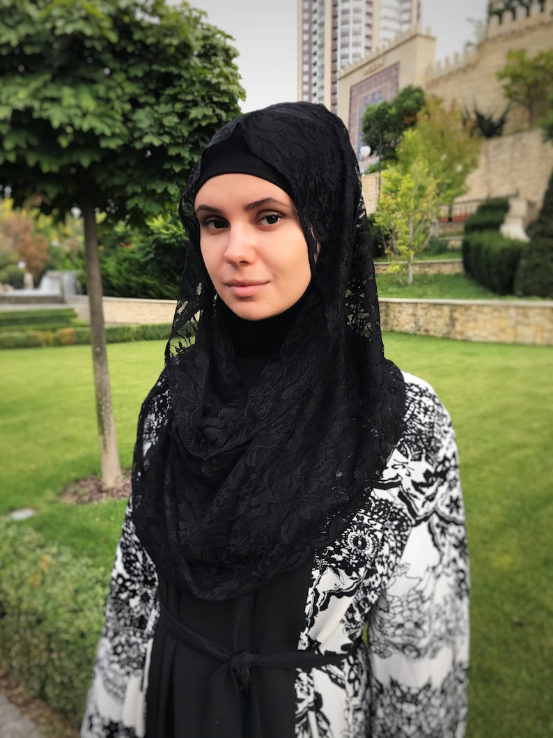 May include: A woman wearing a black lace hijab and a black and white patterned abaya.