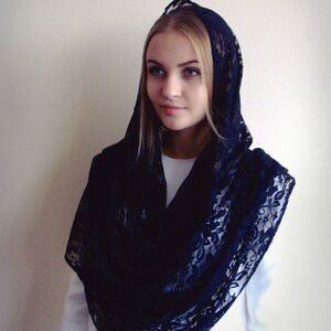 May include: A black lace shawl with a floral pattern. The shawl is draped over a person's head and shoulders.
