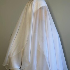 Op de afbeelding: Een witte, doorschijnende sluier met een gegolfde rand. De sluier is over het hoofd en de schouders van een mannequin gelegd en bedekt het gezicht.