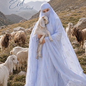 May include: A light blue head covering and matching long dress with delicate floral embroidery, worn with a face veil. The garment features sheer fabric layers. The text "Eid Mubarak" is visible in the upper left corner of the image.