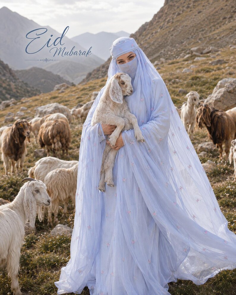 May include: A light blue head covering and matching long dress with delicate floral embroidery, worn with a face veil. The garment features sheer fabric layers. The text "Eid Mubarak" is visible in the upper left corner of the image.