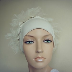 May include: A white fabric head covering with a tulle overlay. The fabric is smooth and has a slight sheen. The tulle is delicate and has a soft, flowing texture.