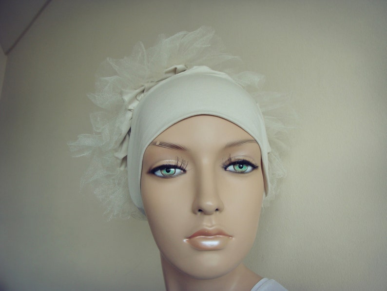 May include: A white fabric head covering with a tulle overlay. The fabric is smooth and has a slight sheen. The tulle is delicate and has a soft, flowing texture.