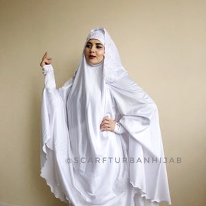May include: White satin hijab with lace trim and a scalloped edge. The hijab is worn over a white underscarf. The text "@scarfturbanhijab" is visible in the lower right corner of the image.